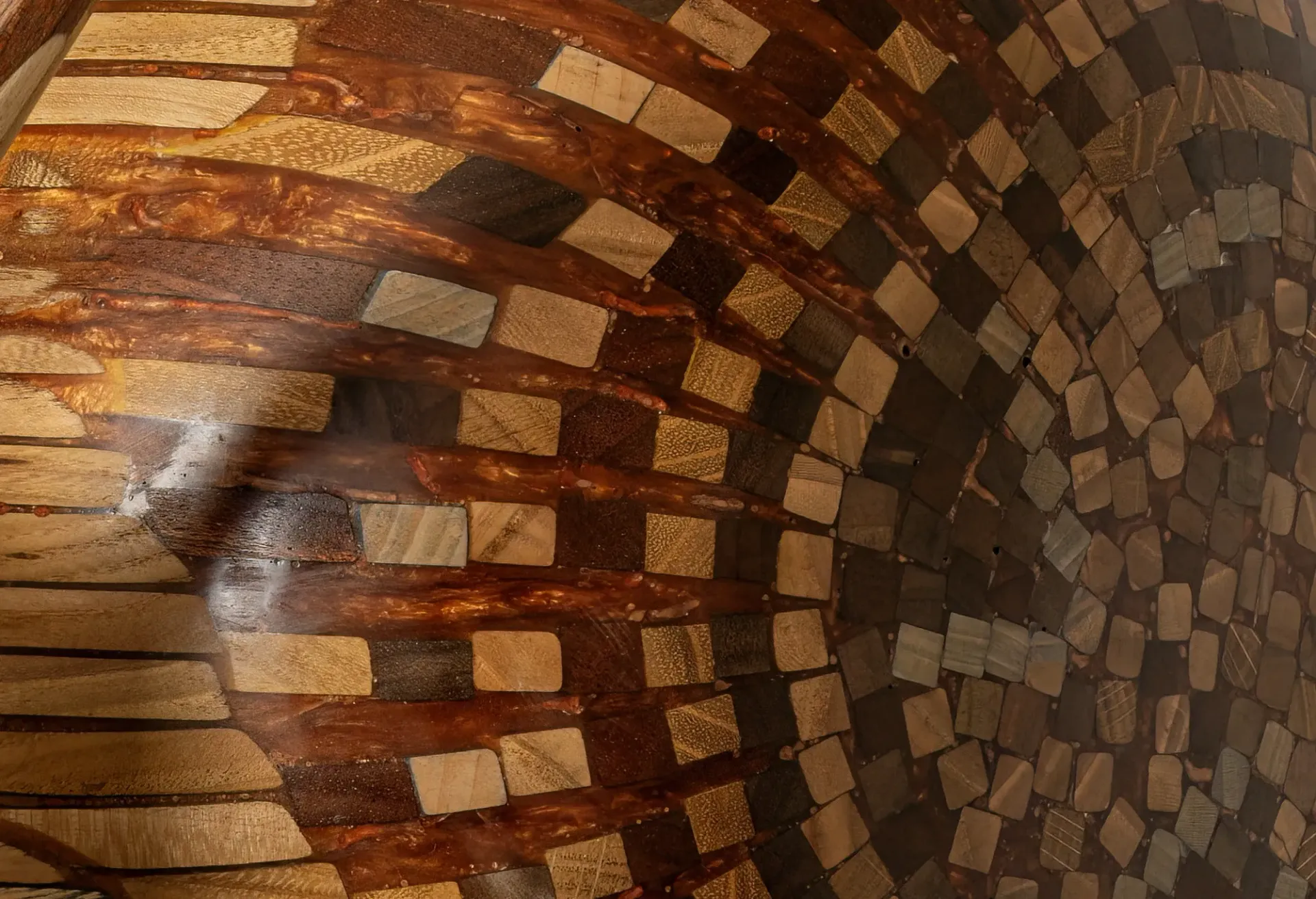 Dettaglio di opera in resina della conchiglia di una chiocciola con mosaico di tasselli di legno. L'illuminazione evidenzia la texture unica della tecnica artistica dell'artista-artigiano Guerino Rusconi.