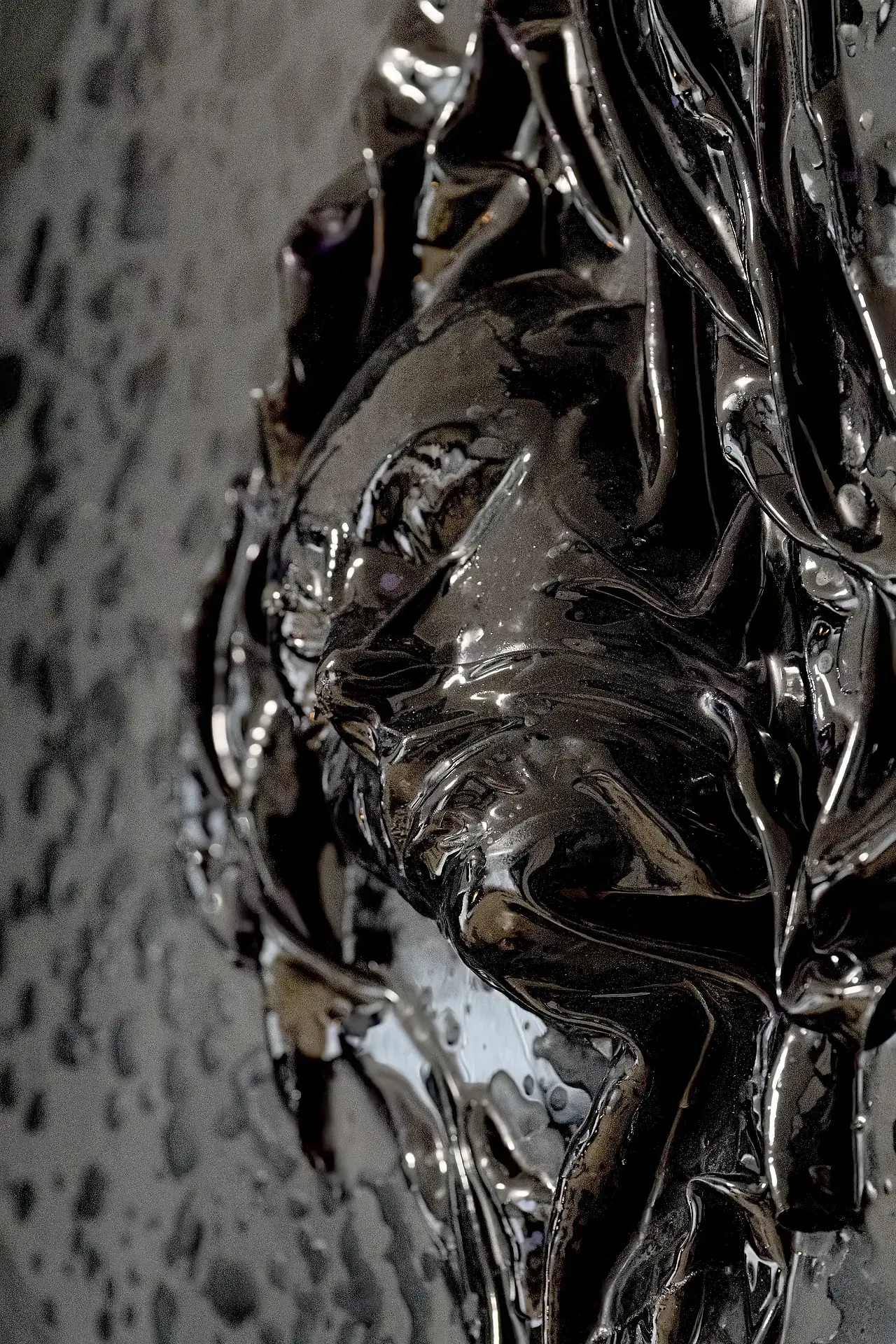 Dettaglio di un'opera in resina epossidica dell'artista italiano Guerino Rusconi, colore nero-grigio carbone scuro, raffigurante un volto umano con drappeggi, sfondo scuro a losanga.