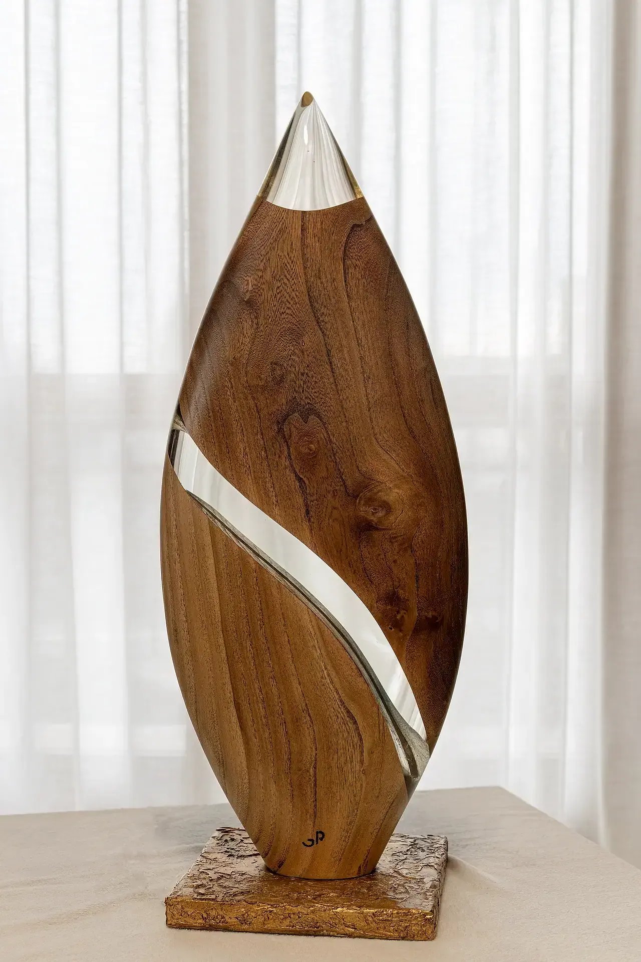 Lampada scultura in resina epossidica trasparente e legno. L'opera ha una forma a goccia con una sezione principale in legno e un inserto curvilineo in resina. La punta superiore è in resina trasparente dove viene emessa la luce. Opera di Guerino Rusconi.