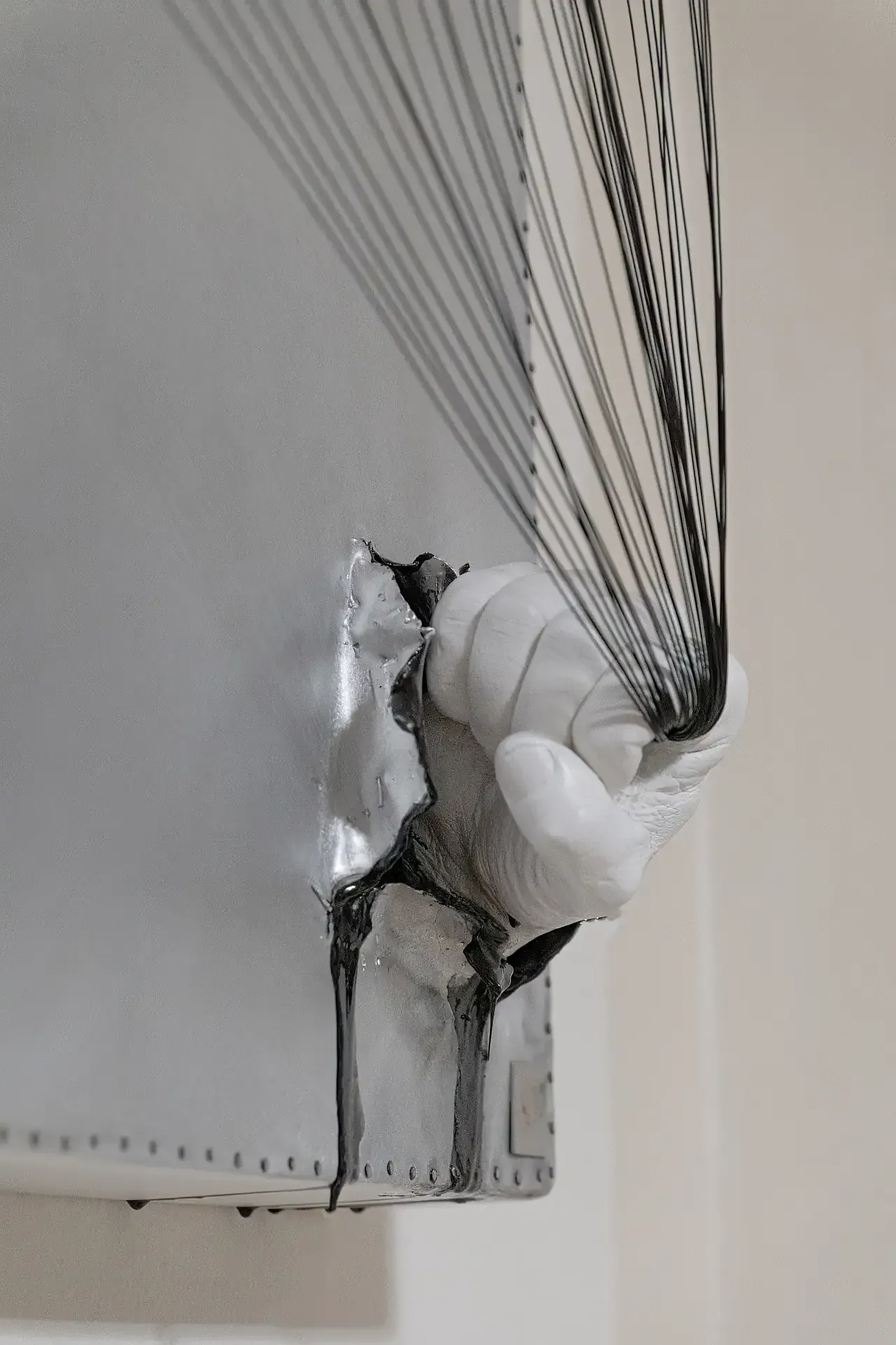 Dettaglio della scultura su tela tridimensionale con tecnica mista raffigurante una mano che impugna fili di alluminio nero. L'opera include colori argento e nero. Opera di Guerino Rusconi.