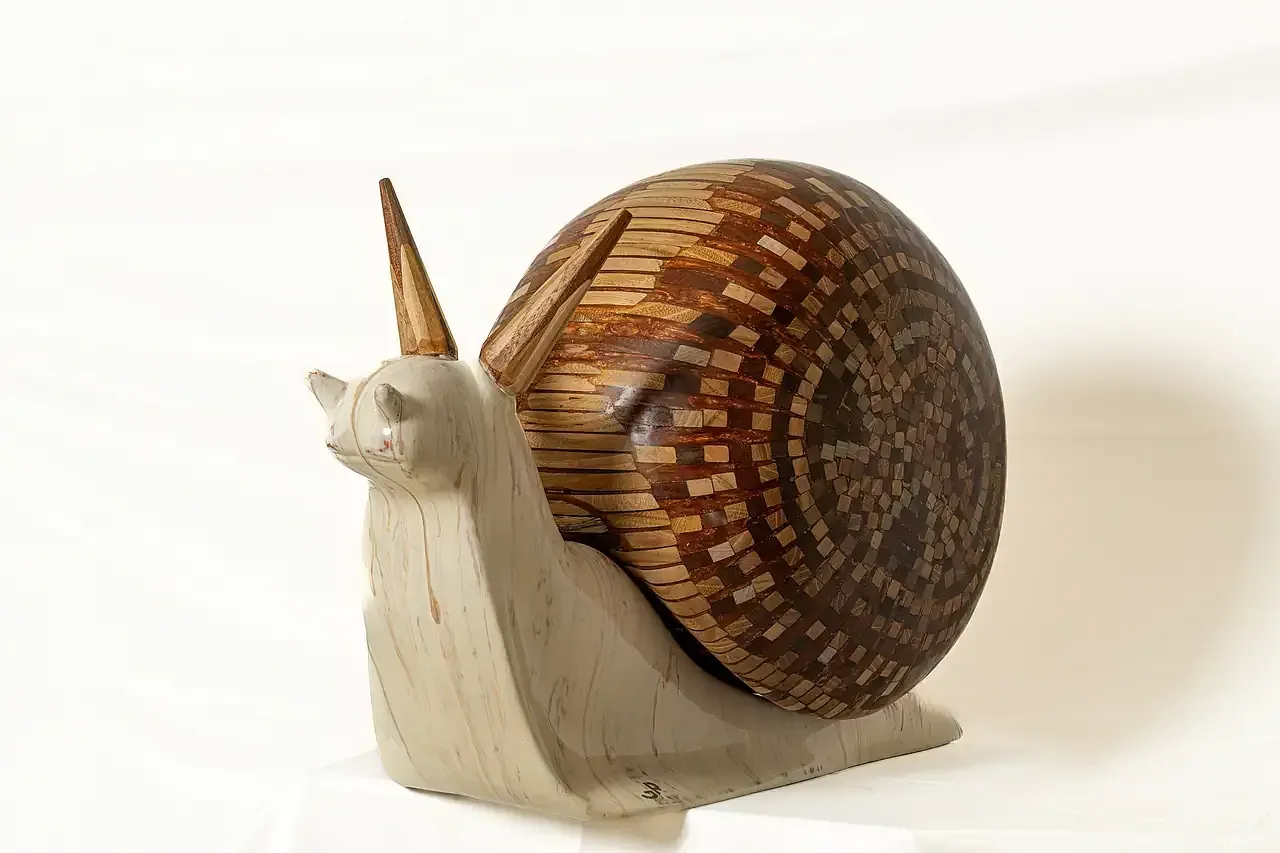 Inquadratura a tre quarti della scultura di chiocciola in resina, gesso ceramico e tasselli di legno dell'artista Guerino Rusconi. Guscio a mosaico in legno dalle tonalità marroni.