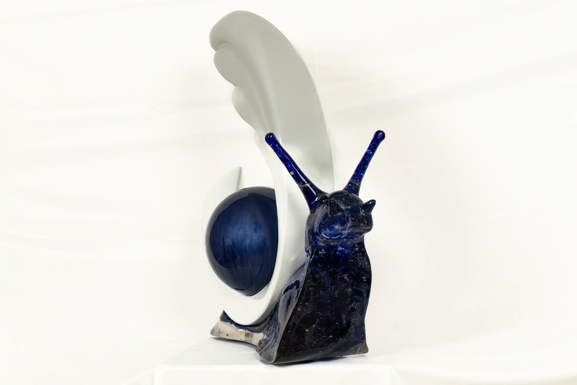 Scultura in resina epossidica raffigurante una chiocciola. Il guscio a forma di sfera in resina è sostenuto e avvolto nella parte inferiore da un dettaglio in gesso ceramicato. Opera di Guerino Rusconi.