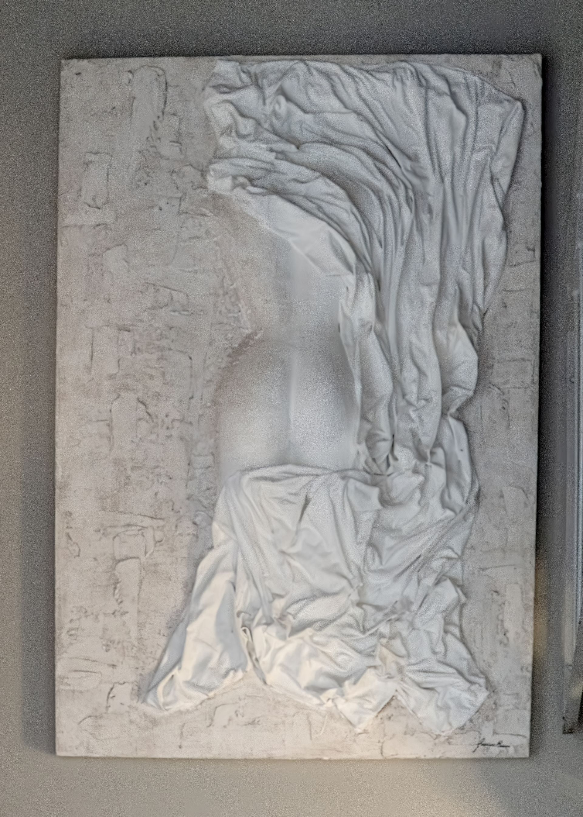 Scultura in resina e gesso ceramico su pannello ligneo. L'opera, realizzata dall'artista Guerino Rusconi, raffigura un corpo femminile visto da una prospettiva posteriore. La figura è parzialmente coperta da un drappeggio bianco, creando un effetto di movimento e tridimensionalità.