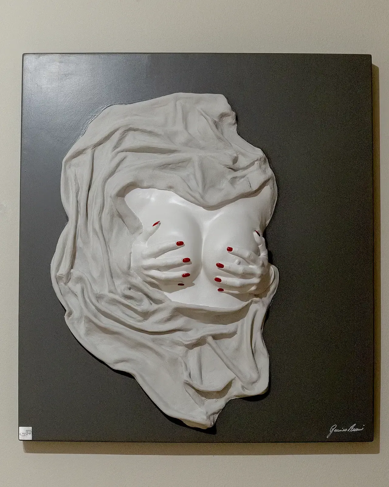 Scultura tridimensionale su pannello ligneo. L'opera raffigura un busto di donna in gesso ceramico bianco che emerge da un drappeggio resinato. Due mani con unghie di colore rosso sorreggono i seni. Opera unica di Guerino Rusconi, artigiano e artista di Soncino.