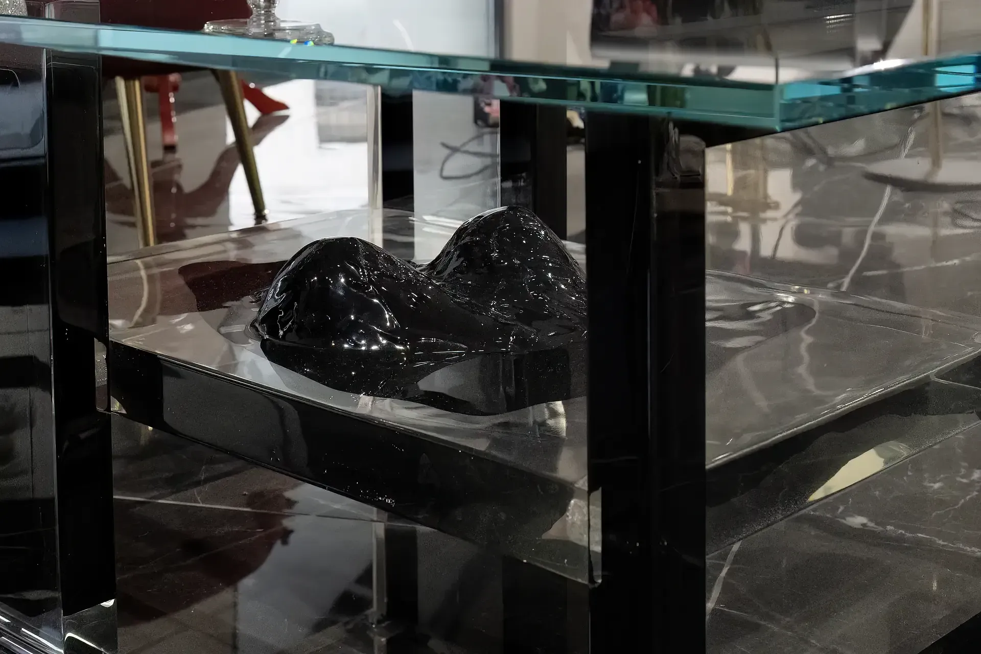 Primo piano del tavolino in resina, posizionata sul ripiano inferiore troviamo un seno femminile tridimensionale. Il dettaglio evidenzia la forma plastica e la superficie materica e riflettente dell'opera di Guerino Rusconi.