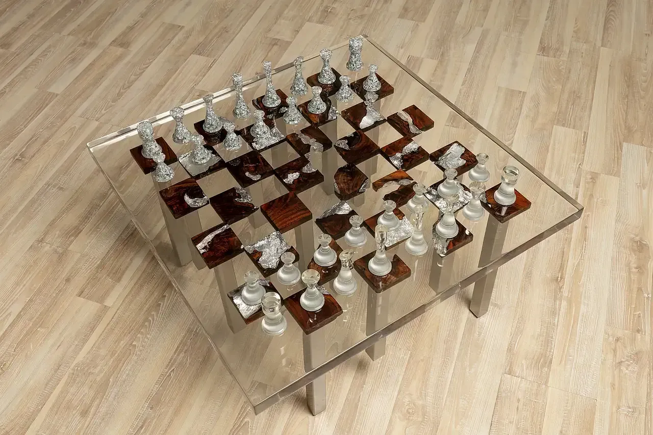 Tavolino-scacchiera realizzato in resina trasparente, con scacchiere alternate in radica di noce con inclusioni di foglie argentate. Pedine della scacchiera in foglia di argento. Gambe del tavolo in acciaio. Opera unica di Guerino Rusconi.