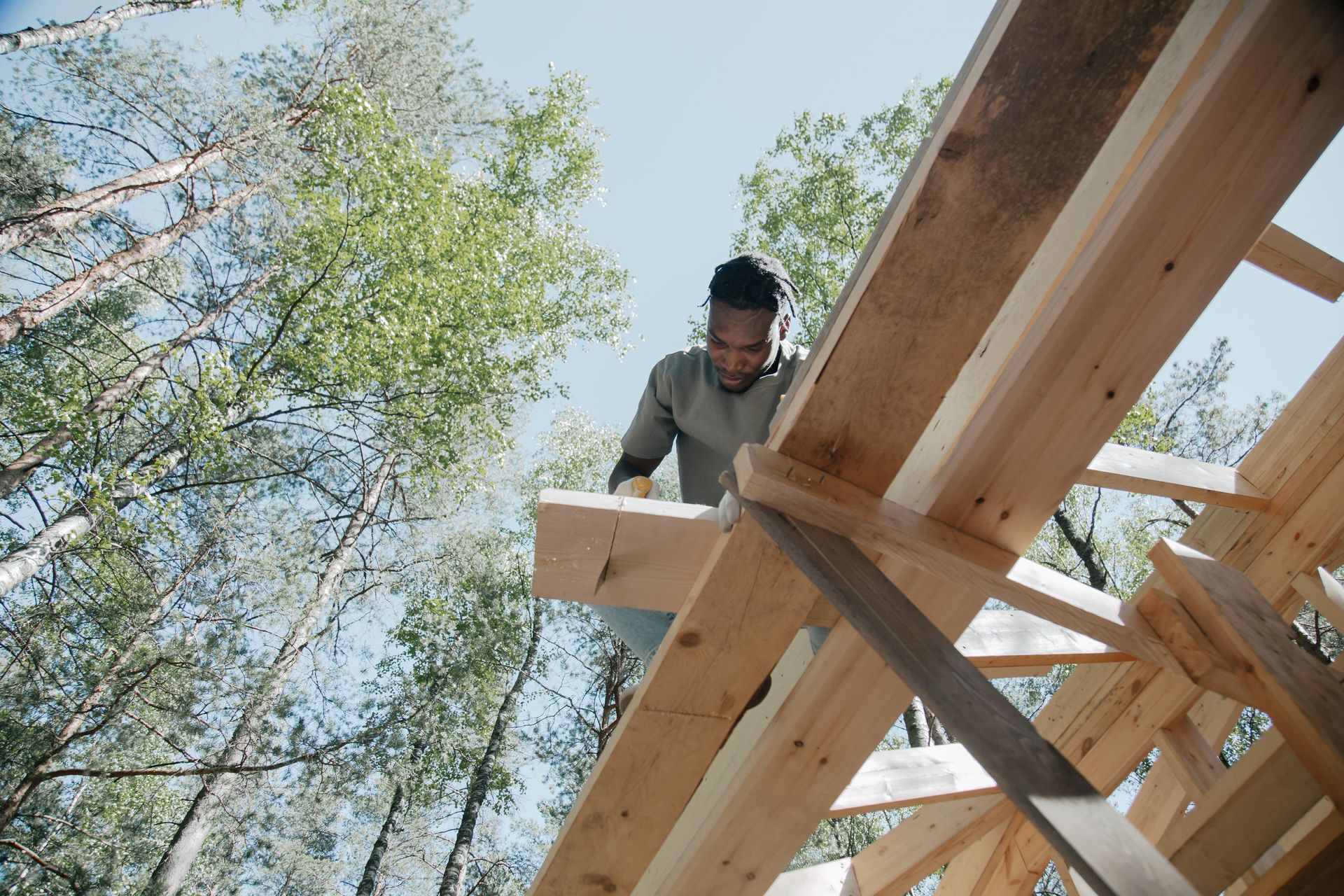 Worker installing wooden beams on a roof frame outdoors under blue sky
