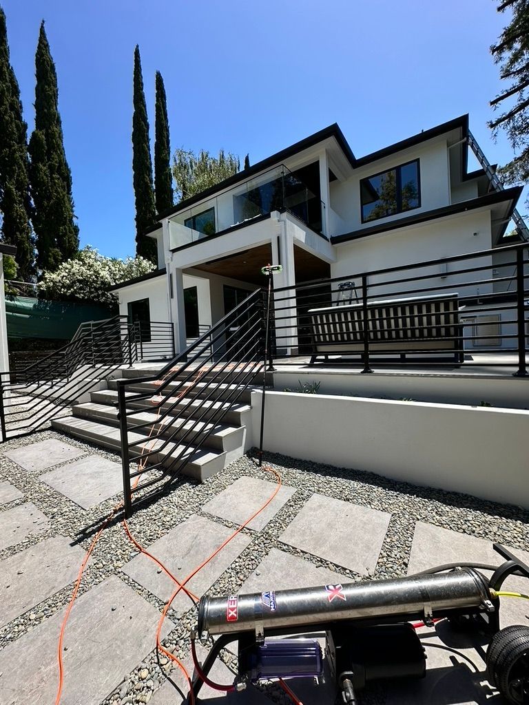 Modern white house with black accents, stone patio, and a large silver device in the foreground.