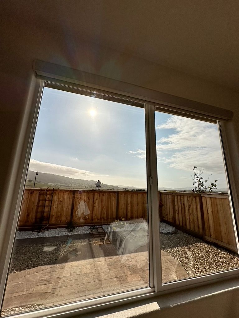 Bright sunlight shines through a window. View of a fence and yard. Mountains and blue sky visible.