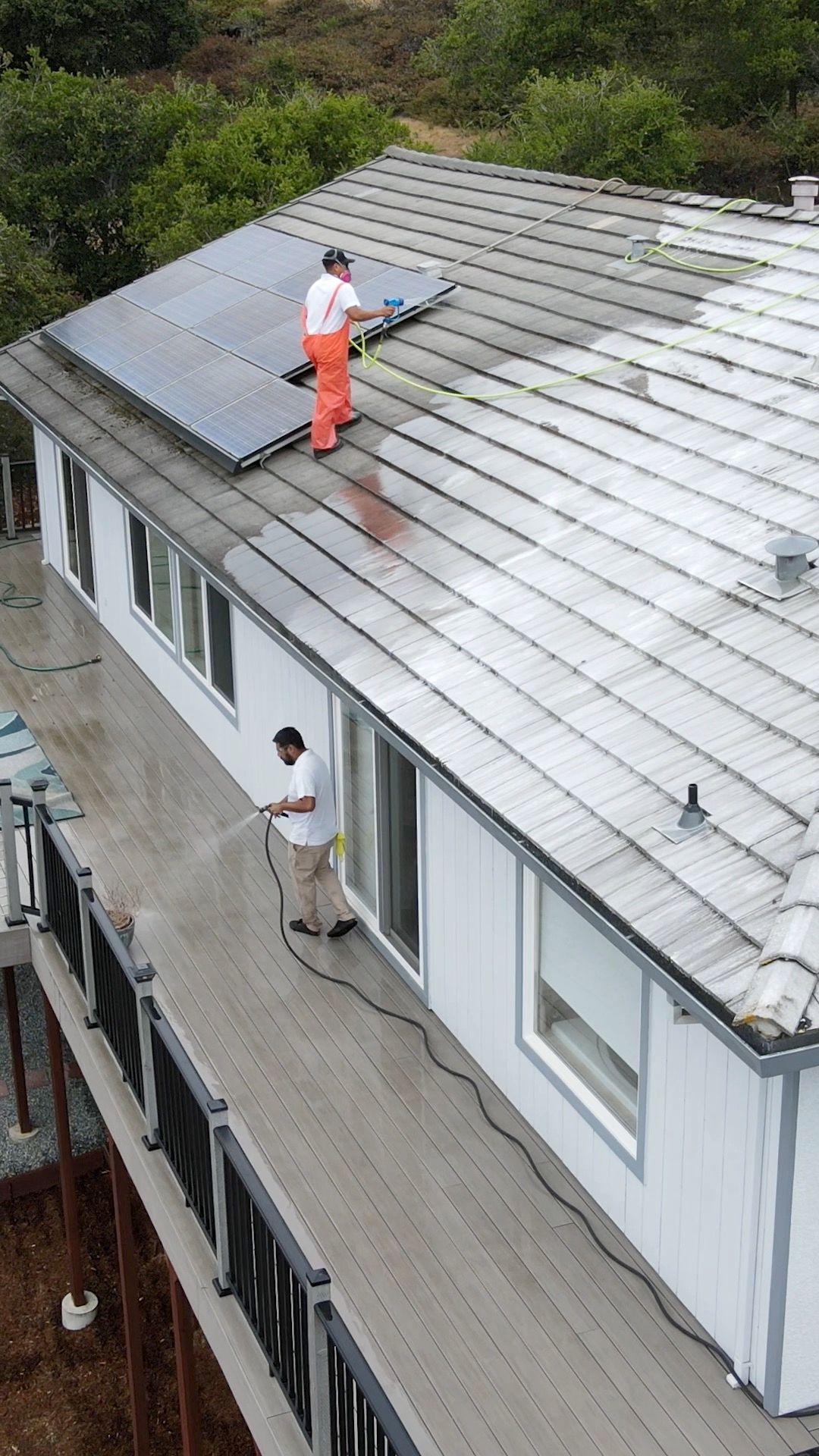 Two men cleaning a house roof. One on the roof, other on the deck.