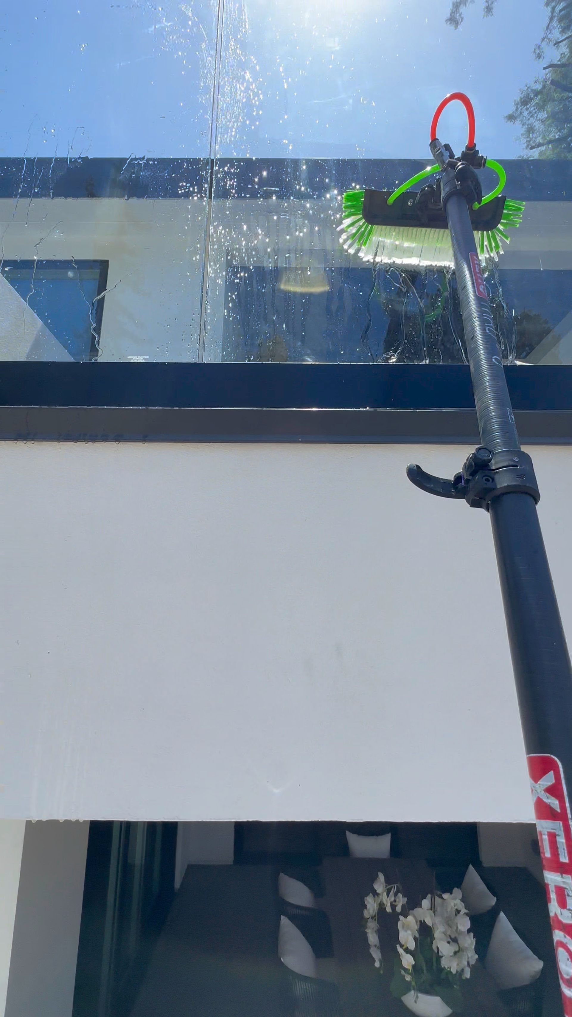 A person cleaning a glass roof with a long-handled brush on a sunny day.