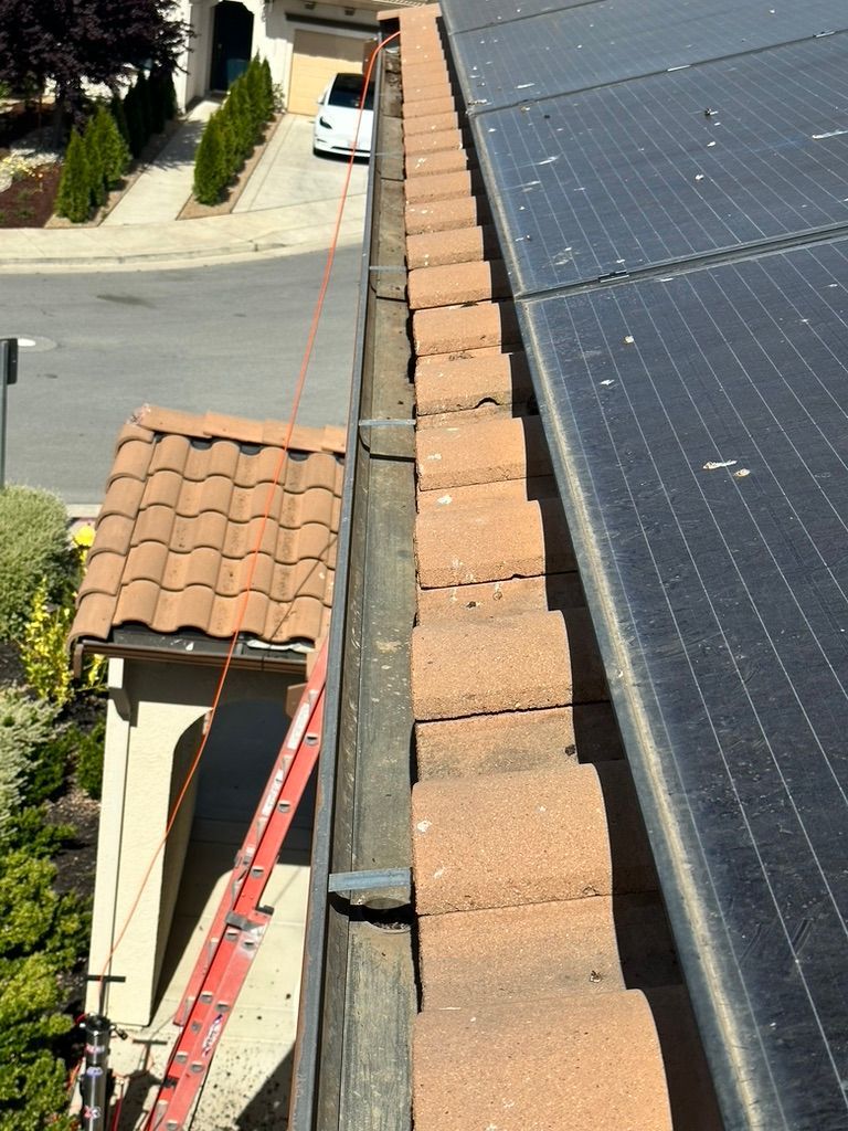 Rooftop with solar panels and terracotta tiles; ladder and safety rope attached.