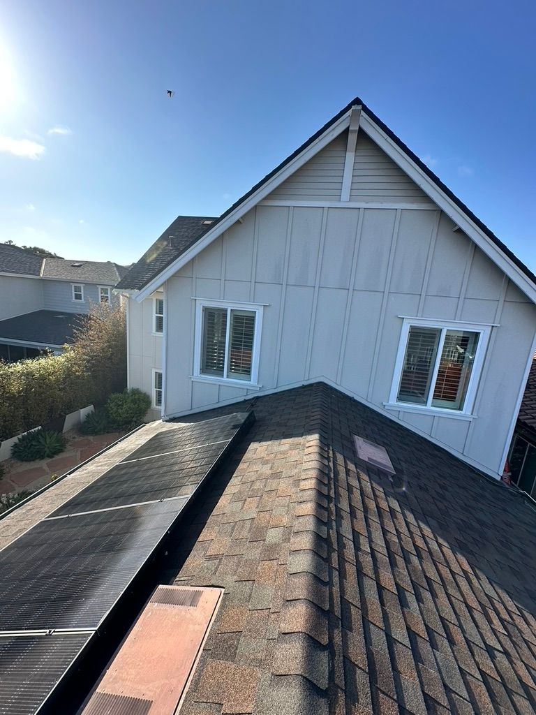 View from a roof, showcasing a two-story house with a dark shingle roof, solar panels, and blue sky.