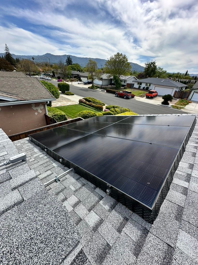 Solar panels on a residential roof, sunny day with a neighborhood street and mountains in the background.