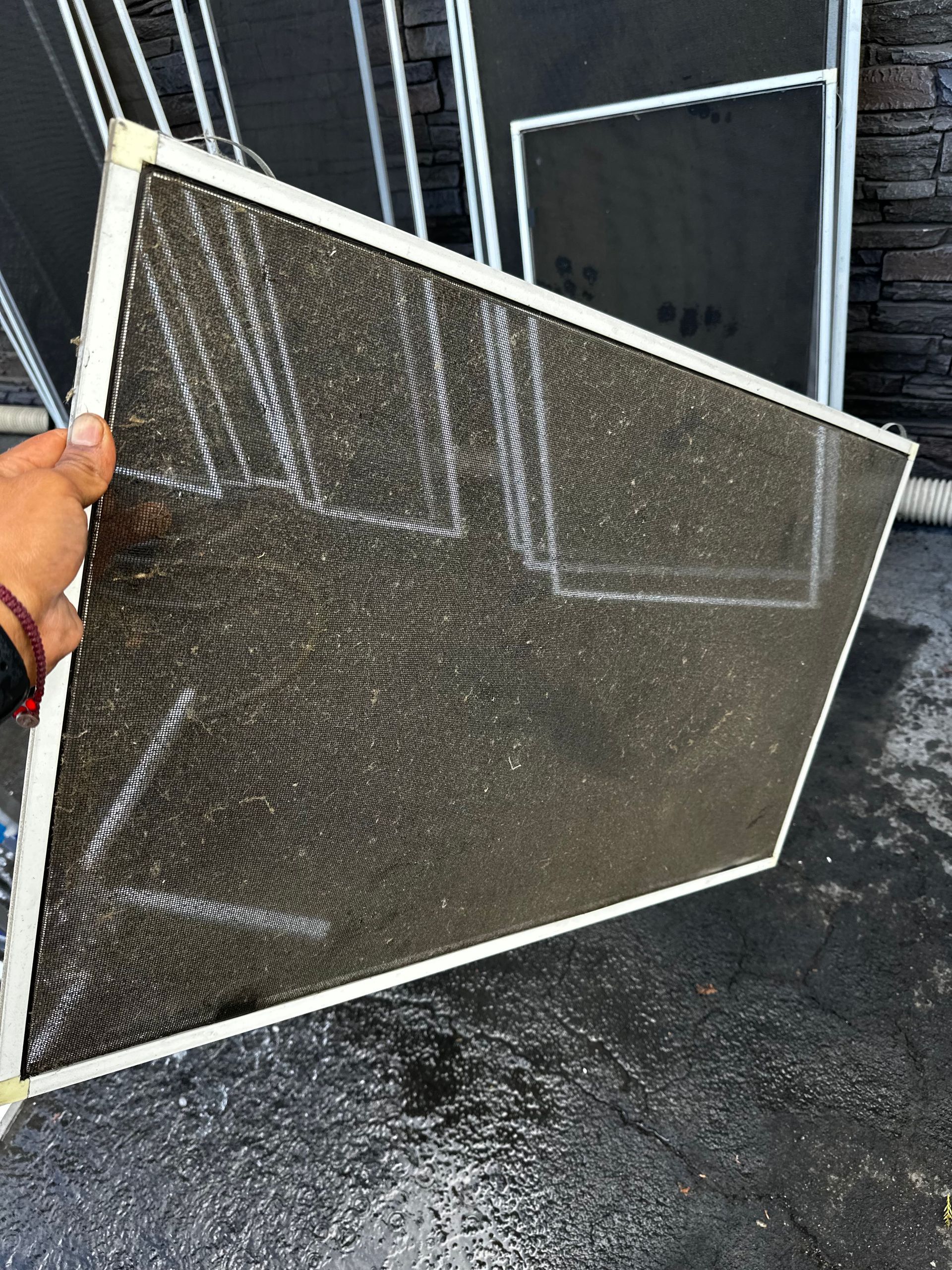 Hand holding a rectangular window screen with dark mesh and a white frame, outdoors.