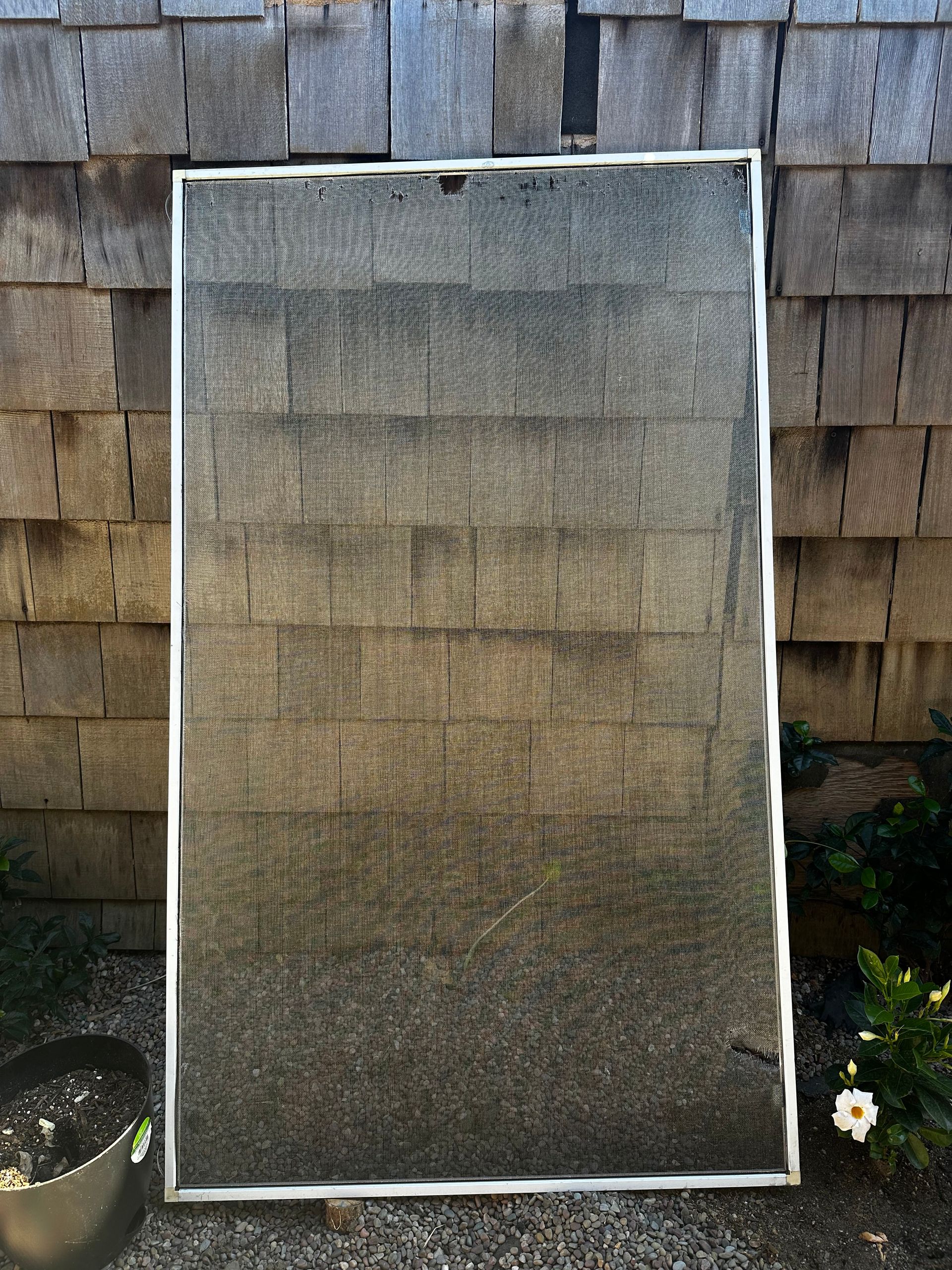 Rectangular screen with gray mesh; against a gray shingle wall, in daylight.