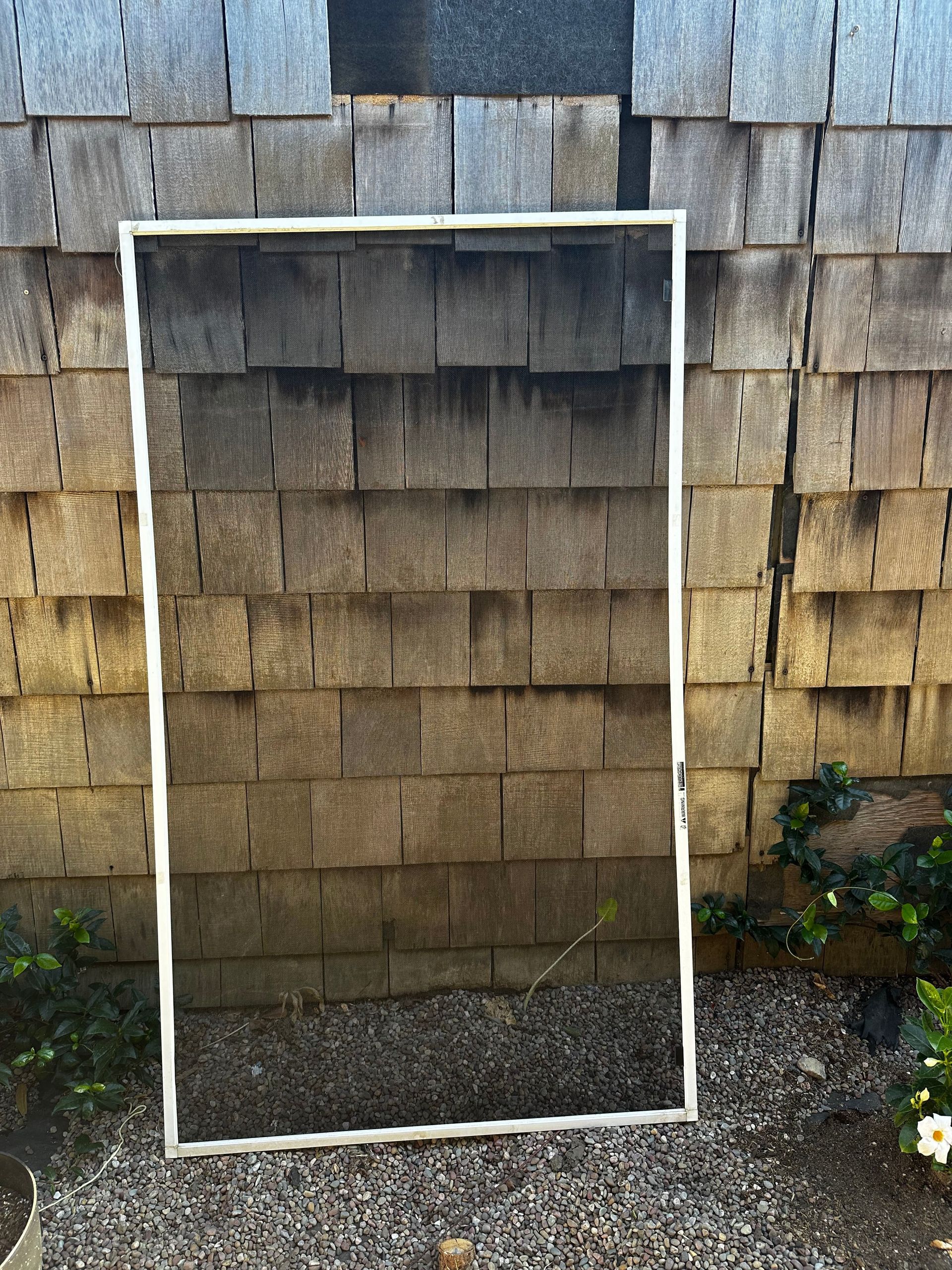 White framed screen leaning against a weathered wood wall.
