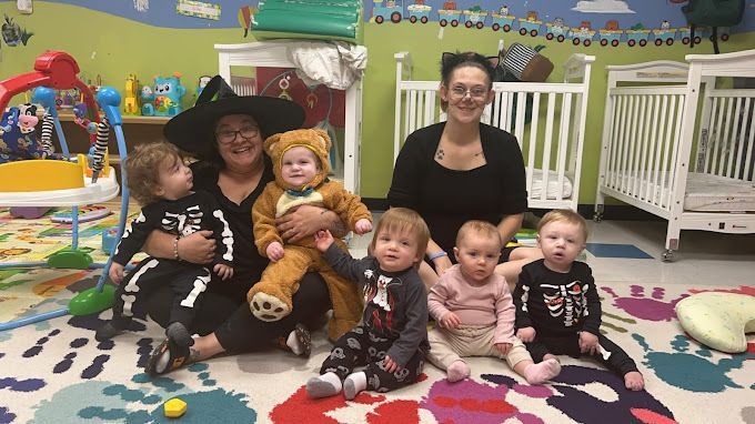 A group of babies and their teachers are sitting on the floor in a room.