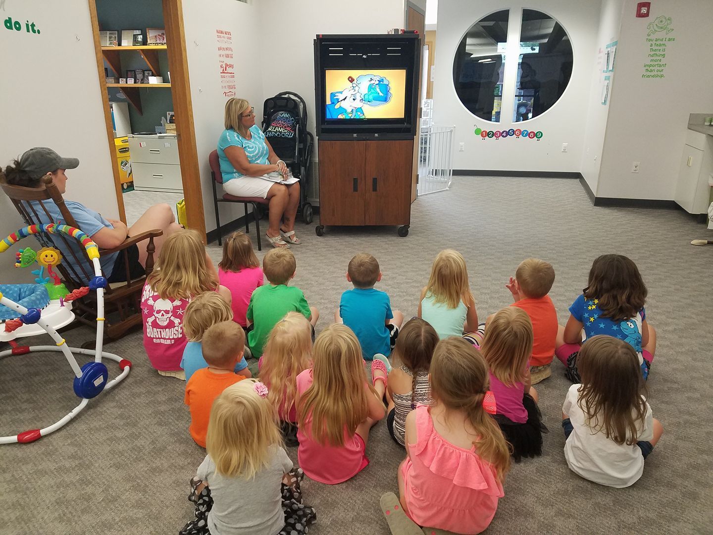 A group of children are sitting on the floor watching a tv