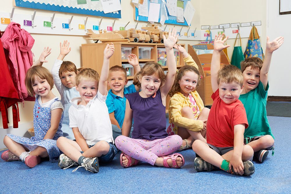 A group of children are sitting on the floor with their hands in the air.