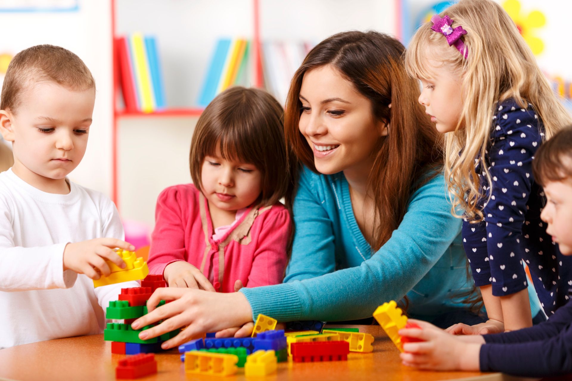Children building with blocks in classroom setting, guided by teacher in early education activity.
