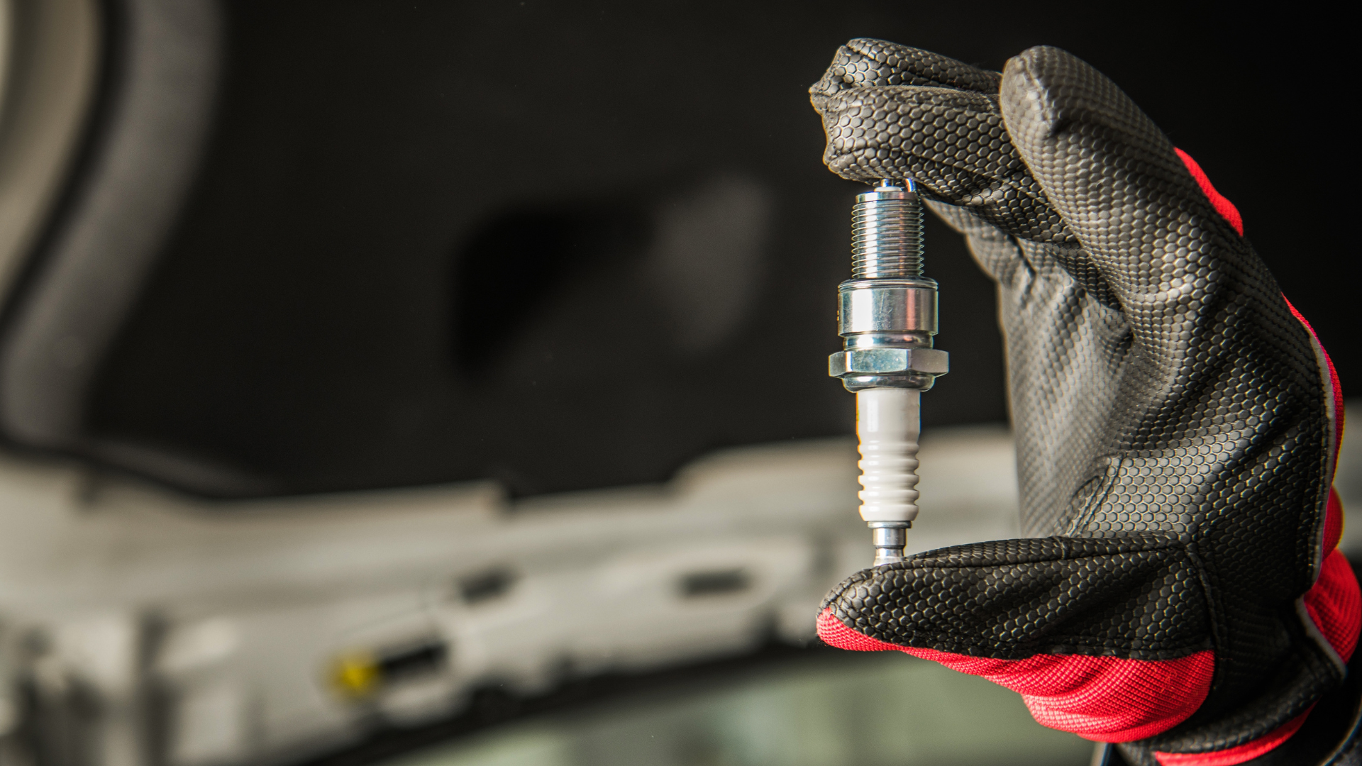 A person wearing gloves is holding a spark plug in their hand.