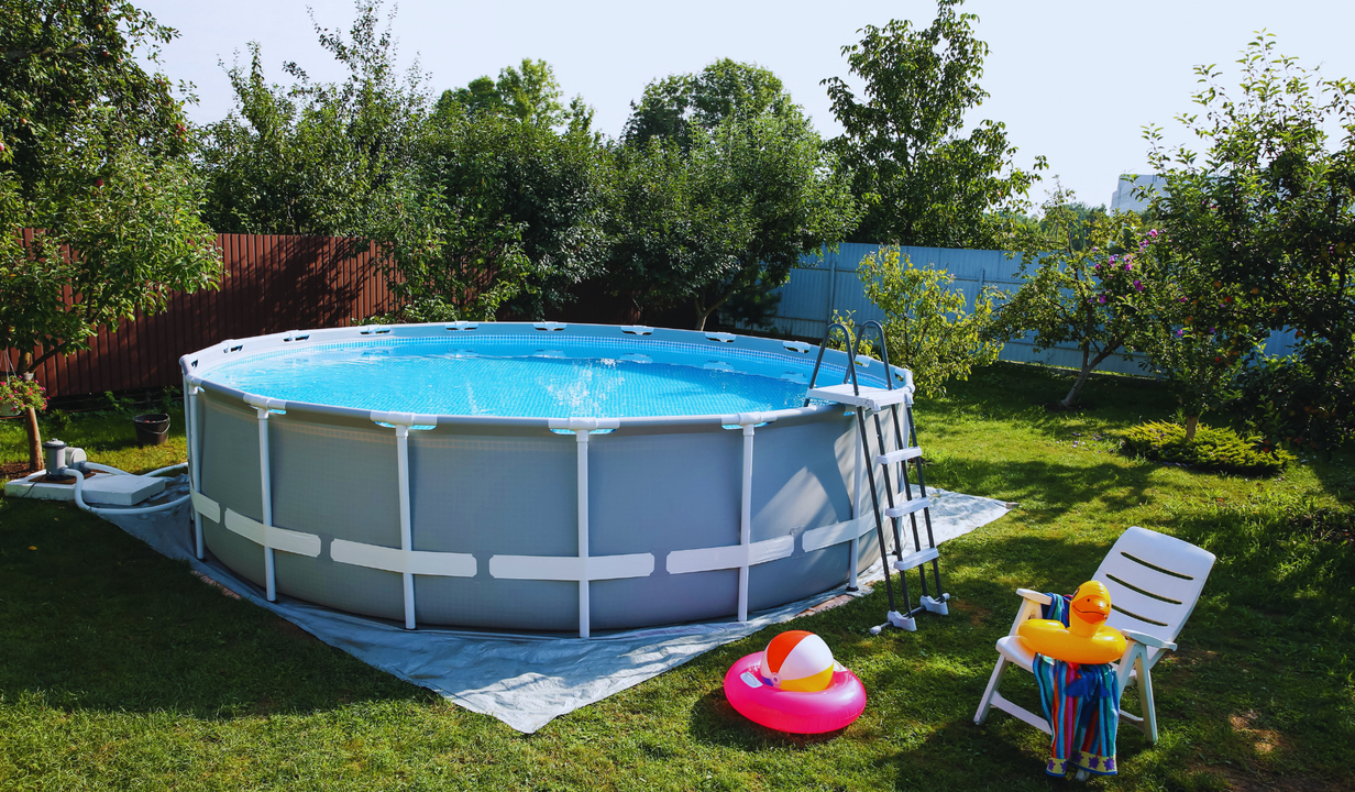 Round above-ground pool filled with water in a backyard. A ladder and accessories like an inflatable ring and chair are nearby.