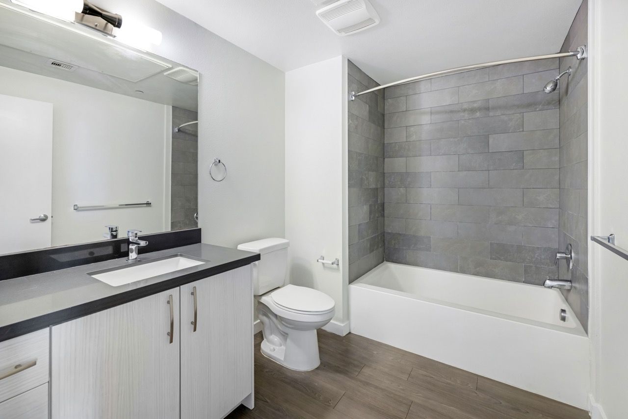 Modern apartment bathroom with vanity, mirror, toilet, and gray tiled bathtub/shower.