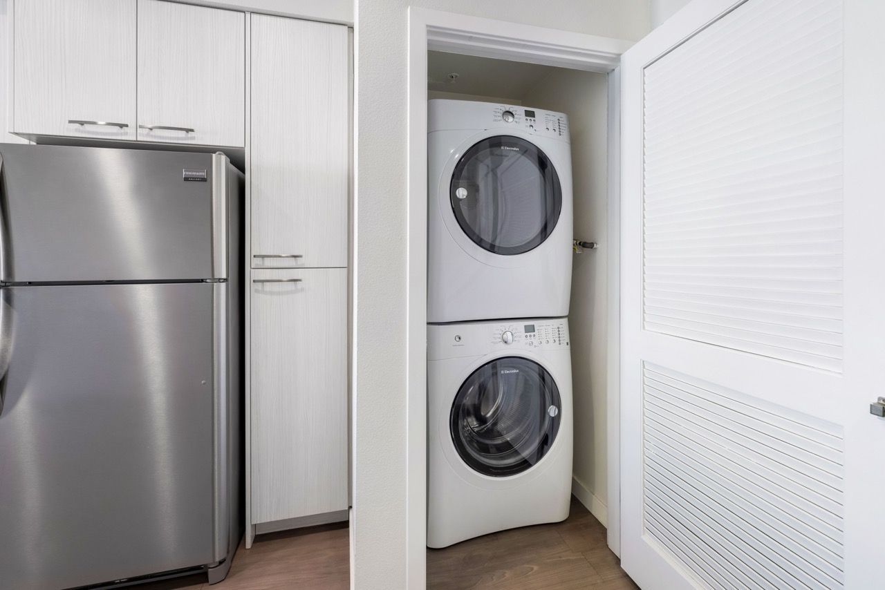 Stacked washer and dryer in a closet beside kitchen cabinets.