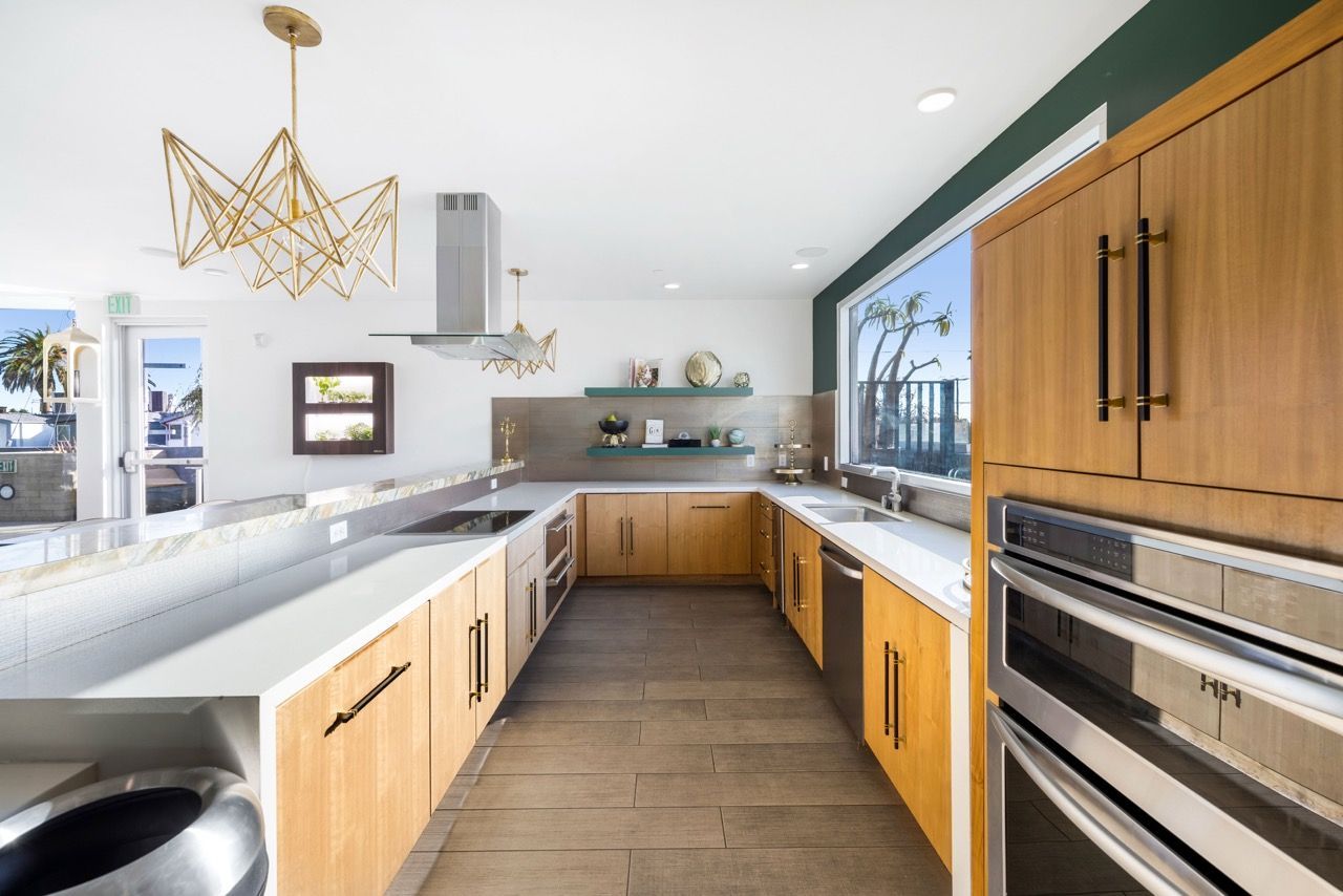 Bright modern kitchen with wooden cabinets, stainless steel appliances, and a large window.