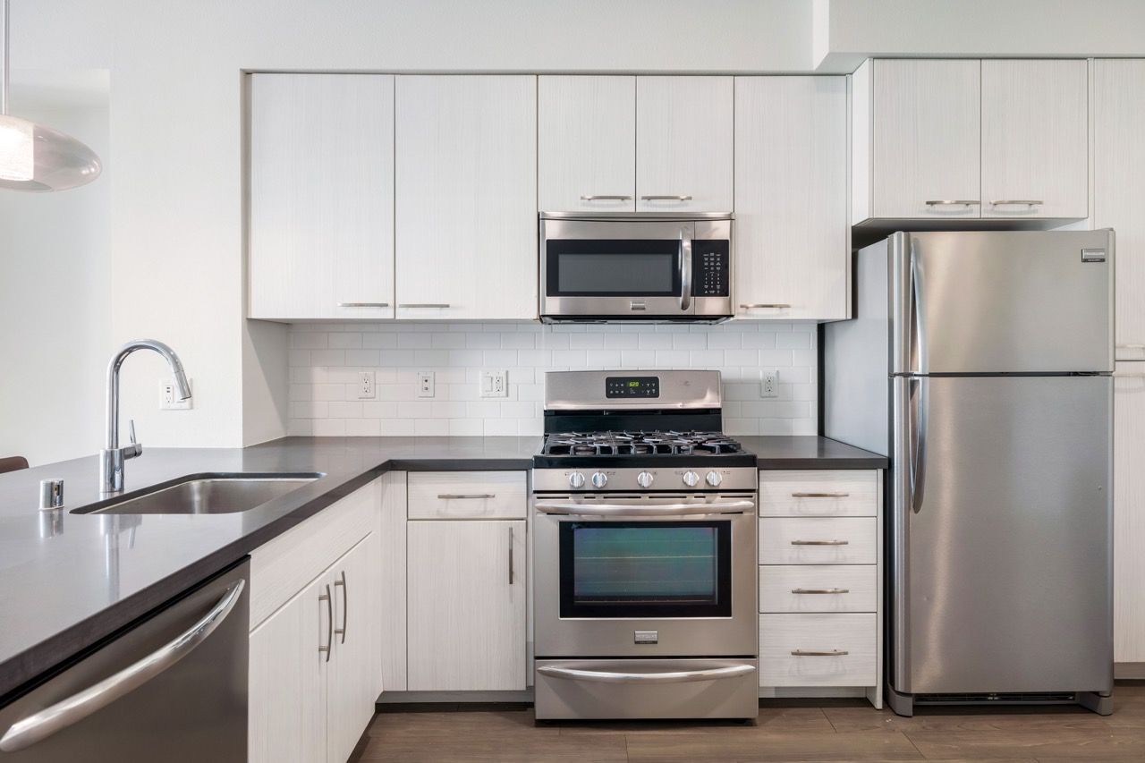 Modern kitchen with stainless steel fridge, microwave, gas range, and white cabinets.