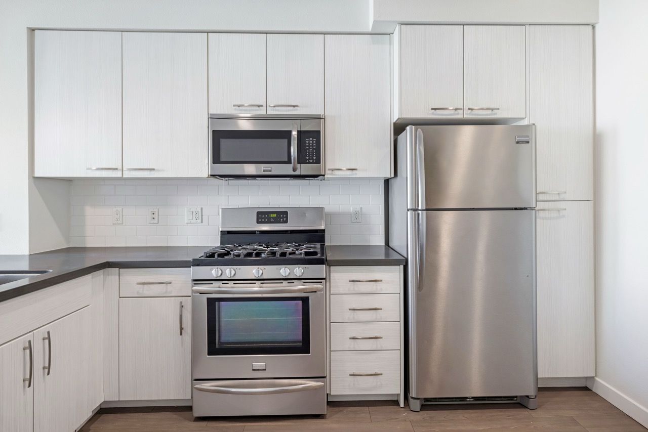 Modern kitchen with stainless steel refrigerator, gas range, microwave, and white cabinets.