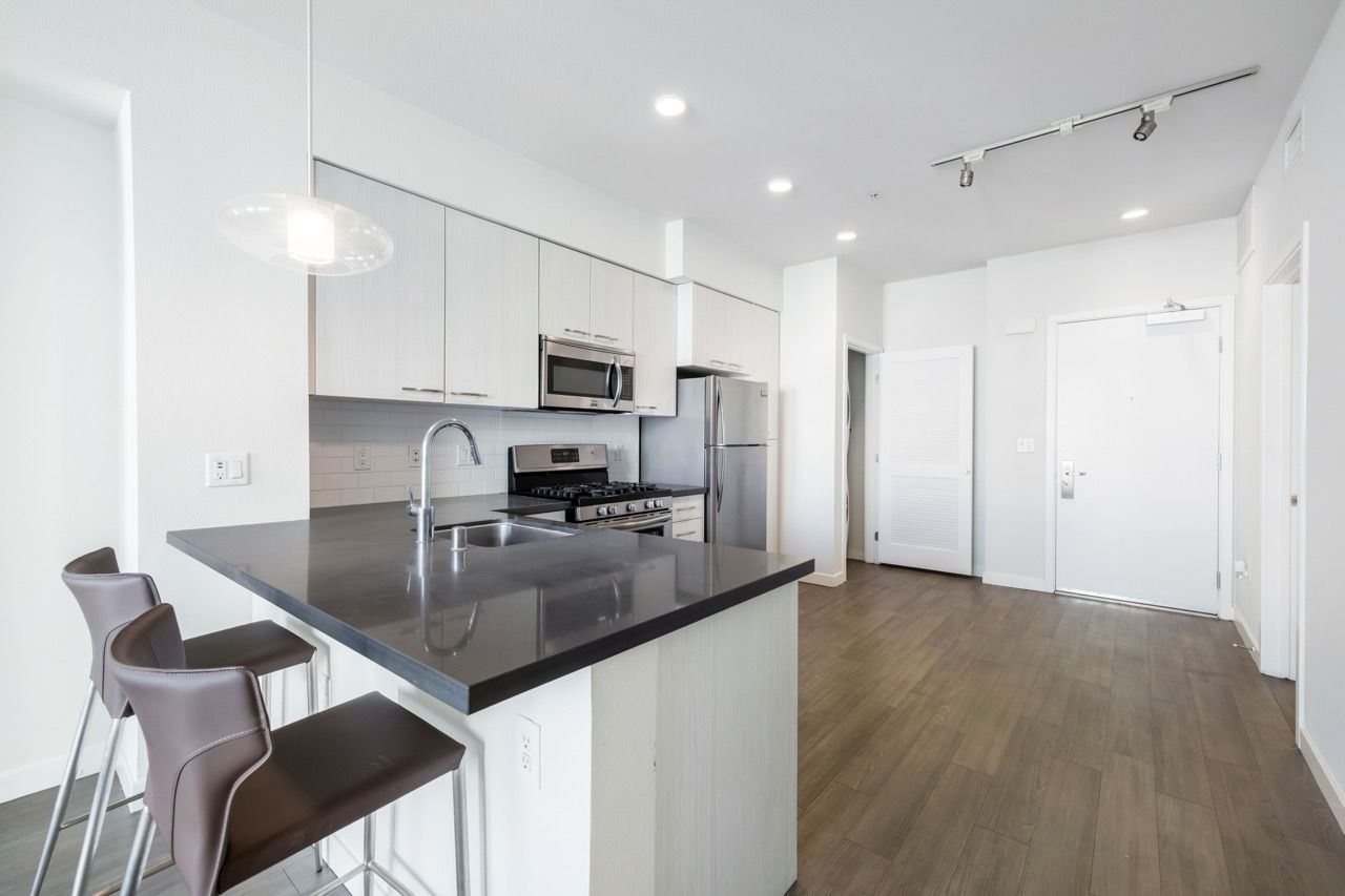 Open-concept kitchen with an island, gray countertop, white cabinets, and stainless steel appliances.