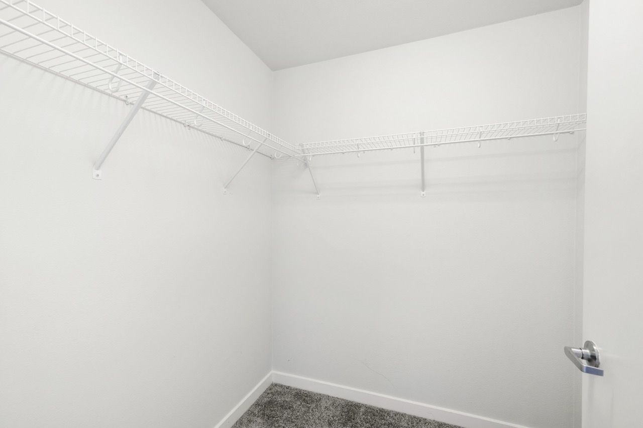 Empty walk-in closet with white wire shelving and gray carpet.