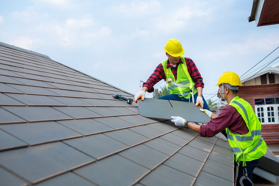 Two construction workers are working on the roof of a house.