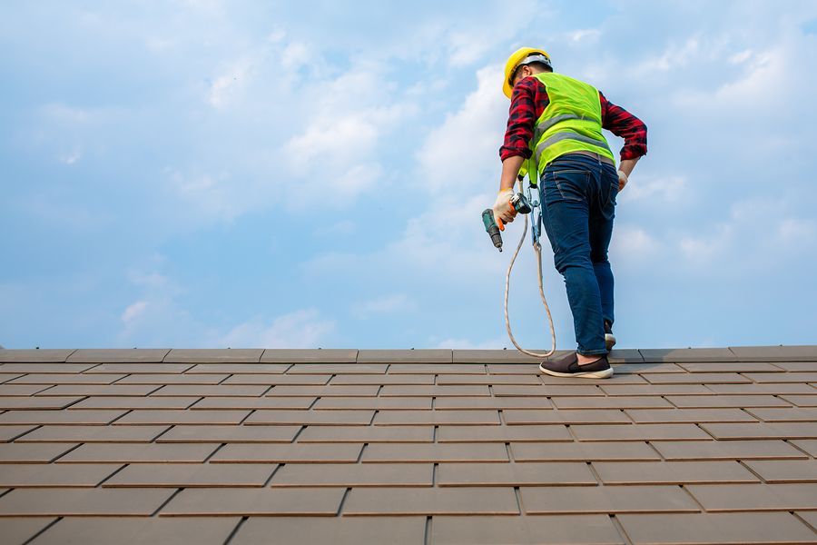 A man is standing on top of a roof holding a tool.