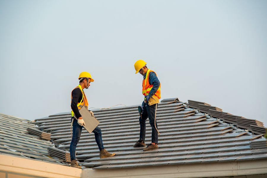 Two construction workers are working on the roof of a house