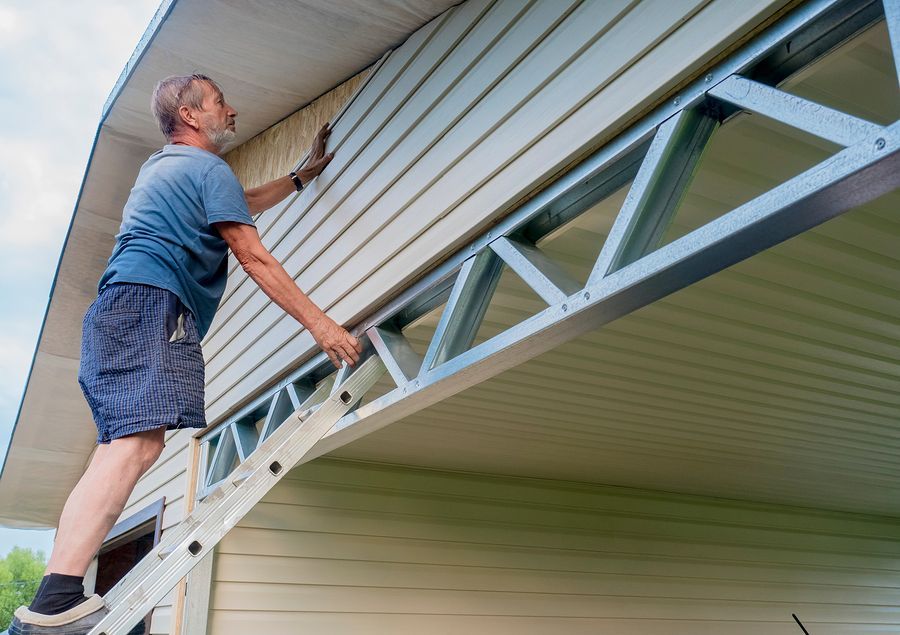 A man is standing on a ladder painting the side of a house.