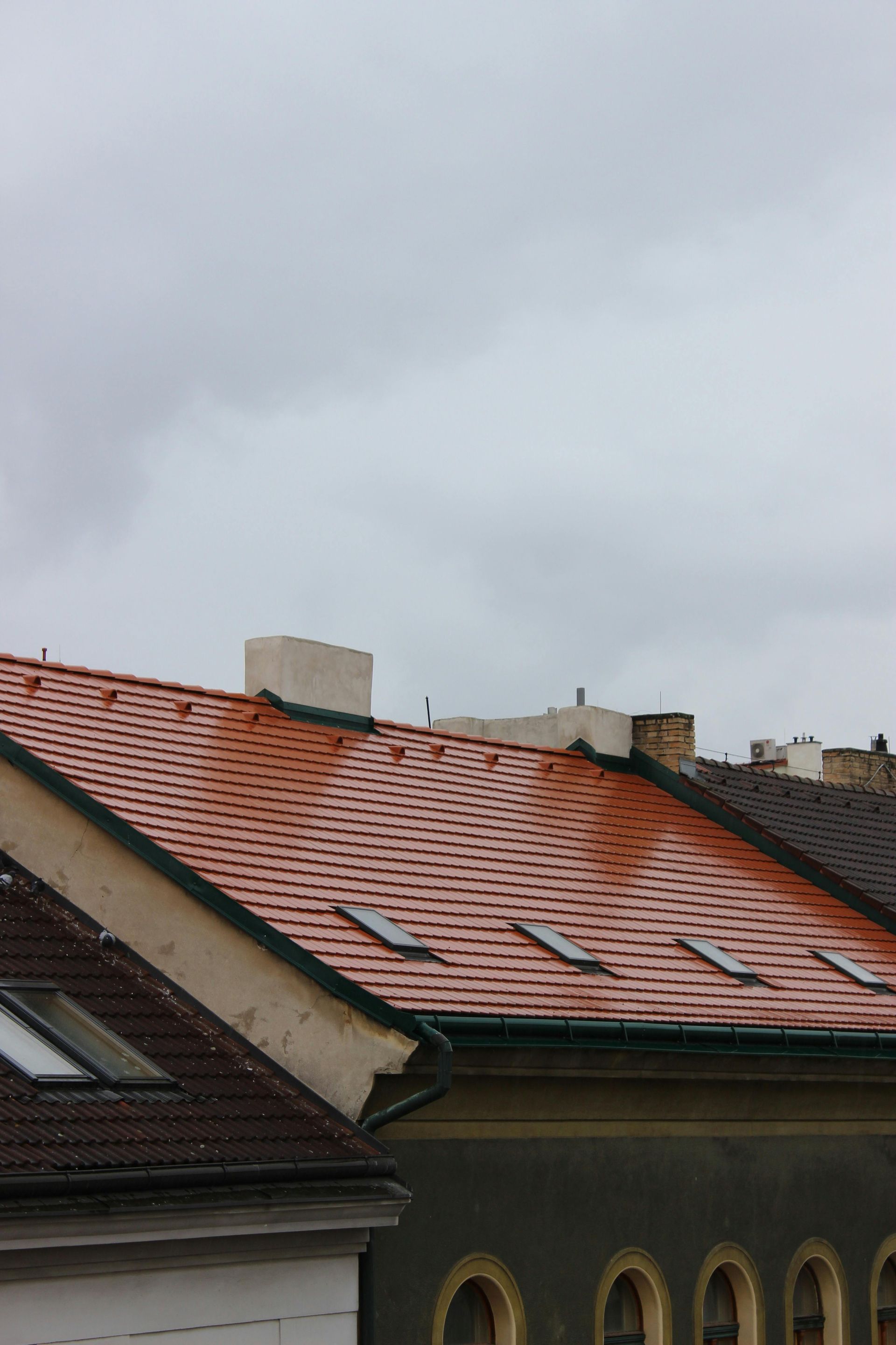Red tiled rooftop with skylights, gray sky.