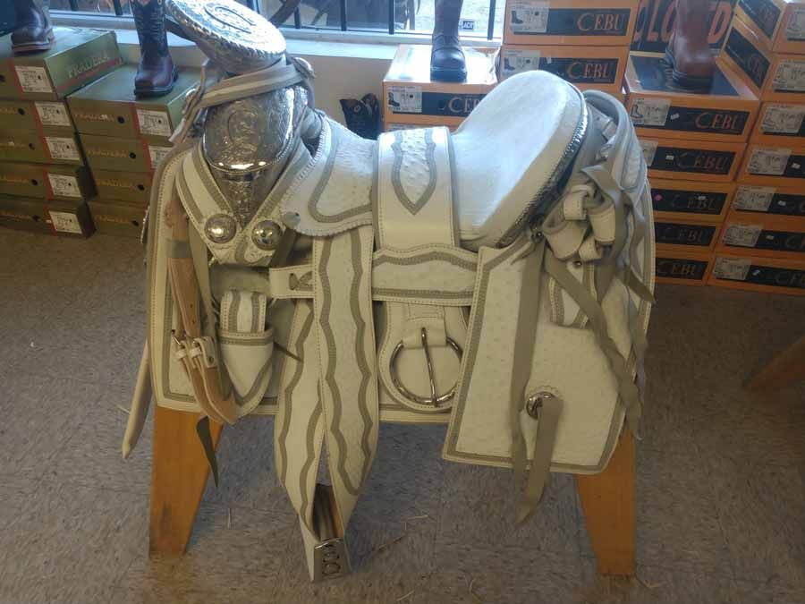 White-and-silver ornate saddle on a wooden stand in a tack shop.