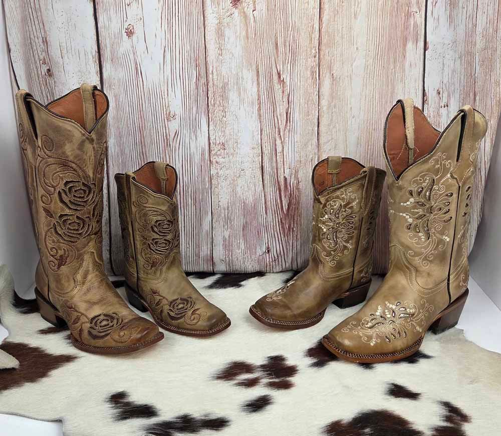 Four pairs of ornate tan and gold cowboy boots arranged on a rustic wood backdrop.