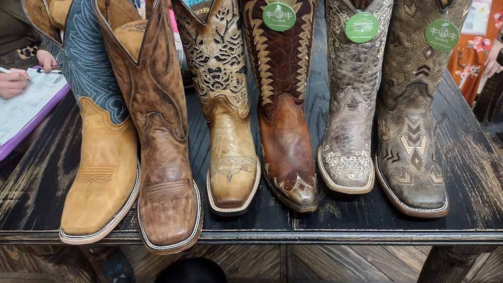 Row of Western-style cowboy boots in tan, brown, leopard print, and gray on a store display shelf