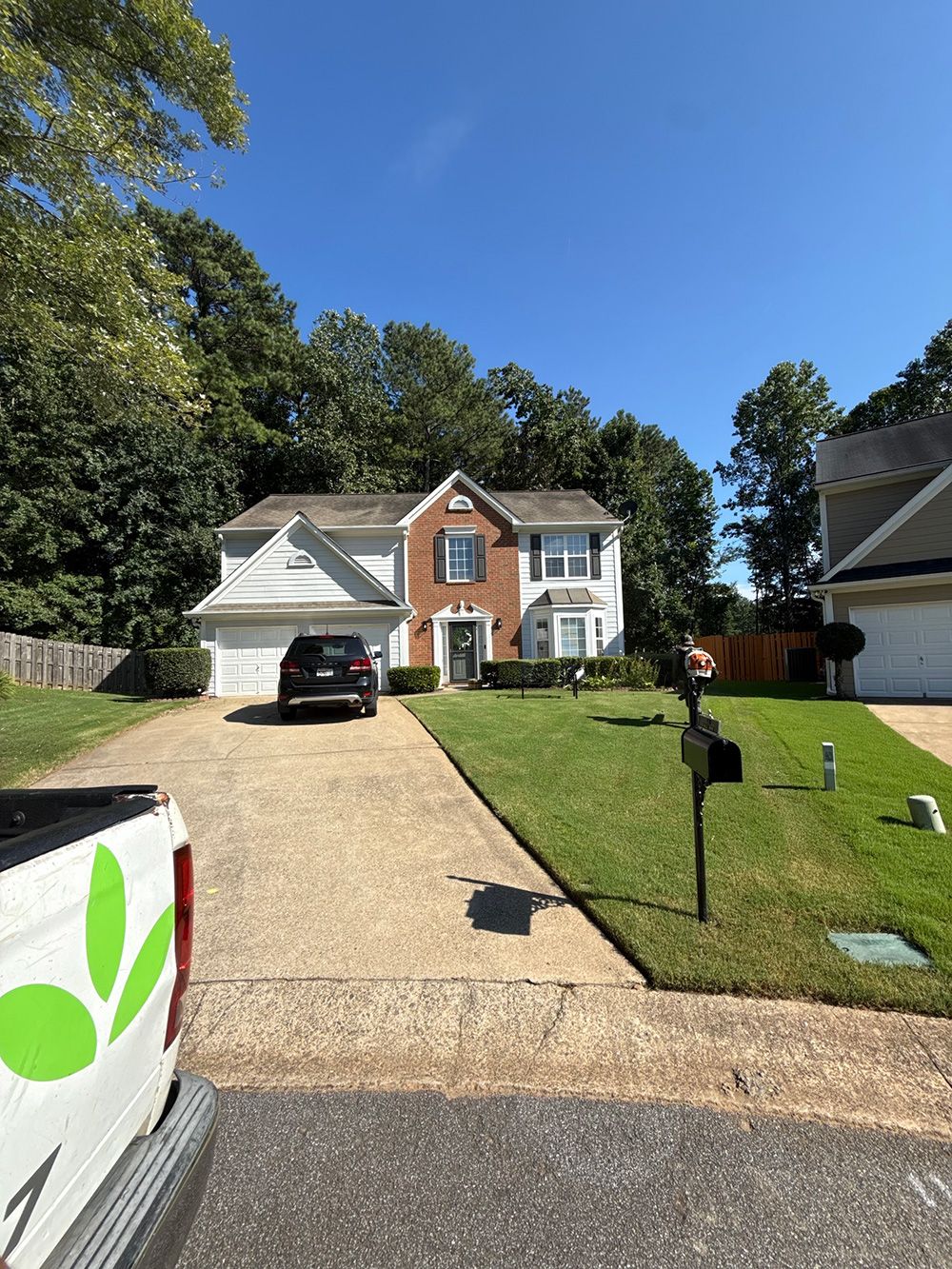 Two-story house with a brick facade and attached garage, with a driveway and green lawn on a sunny day.