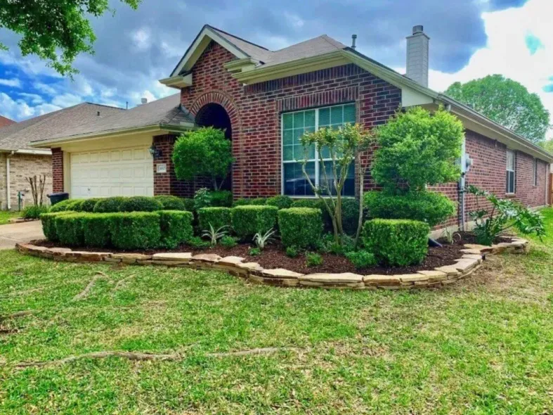 Brick house with manicured green shrubs and stone border in a grassy yard.
