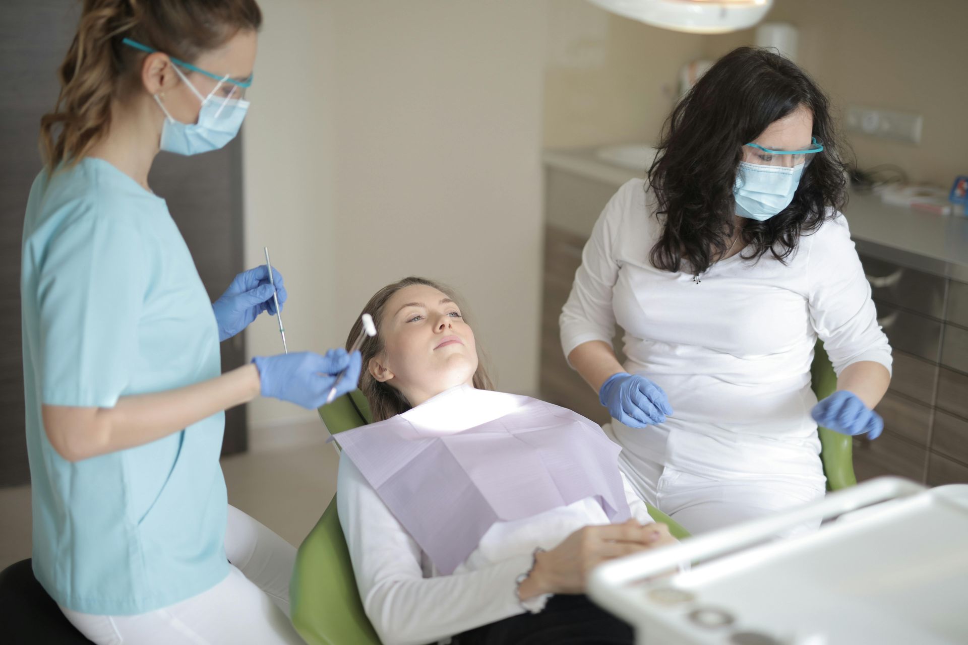 Woman in dentist chair, receiving treatment from two dental assistants.