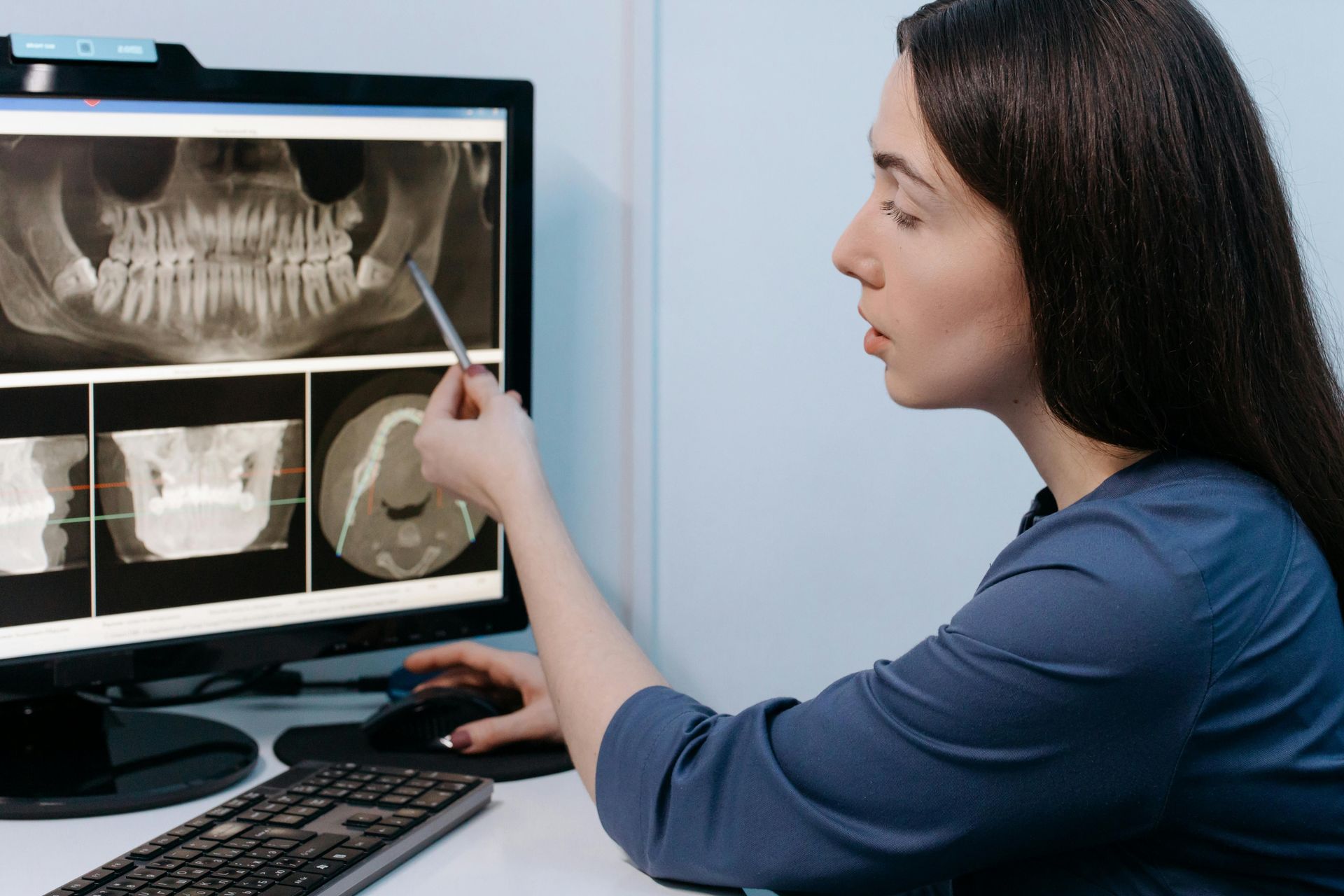 A dental professional pointing at an X-ray on a monitor in an office.