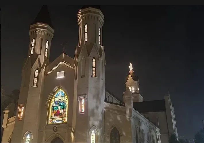 A church with a stained glass window is lit up at night.