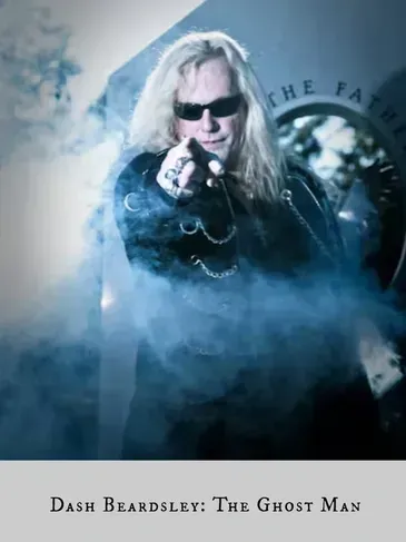 A man with long blonde hair and sunglasses is pointing at the camera.