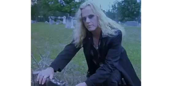 A woman in a black coat is kneeling in the grass in a cemetery.
