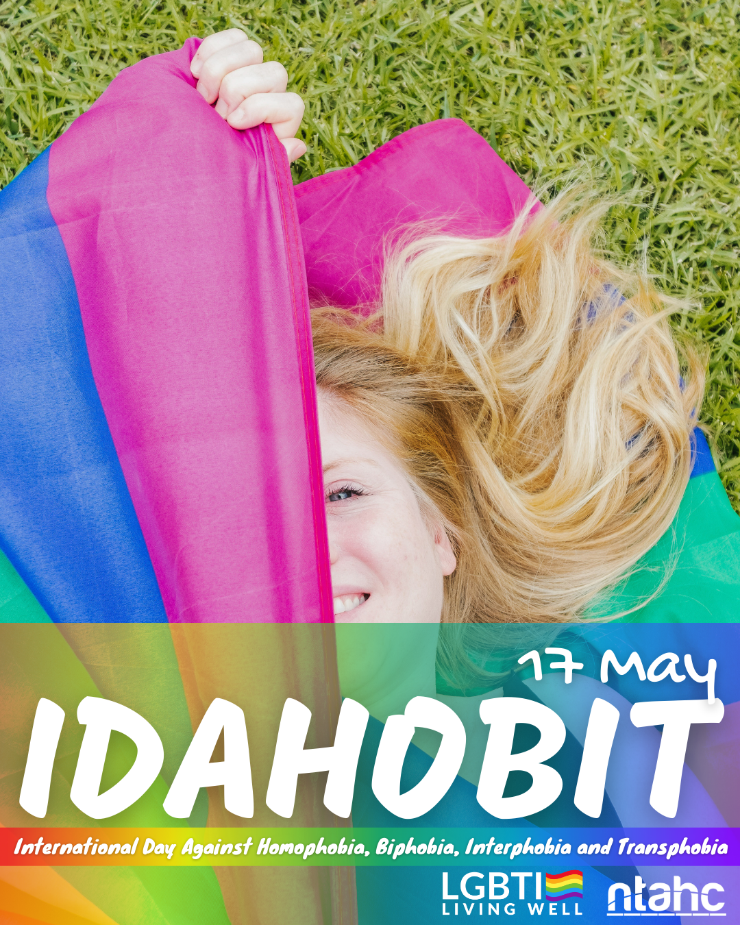 A woman is laying in the grass holding a rainbow flag